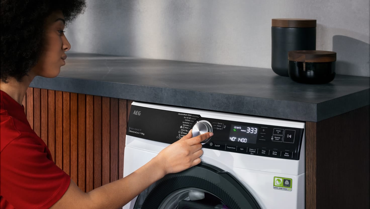 Woman adjusting controls on AEG washing machine.