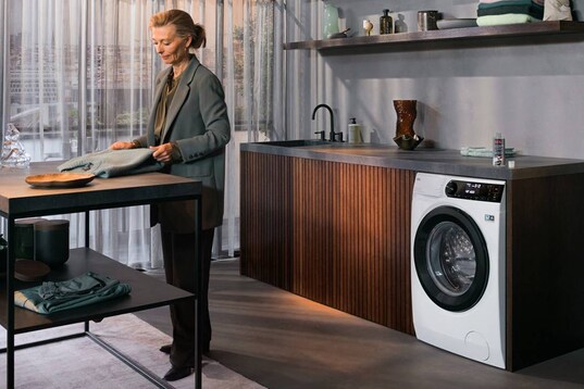 Femme pliant un sweat-shirt dans une buanderie devant un lave-linge séchant