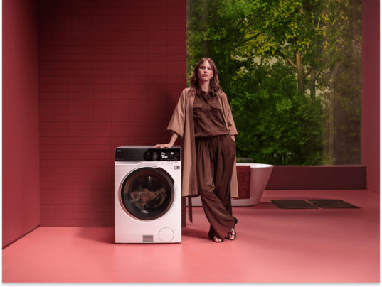 Femme debout à côté d'une machine à laver AEG..